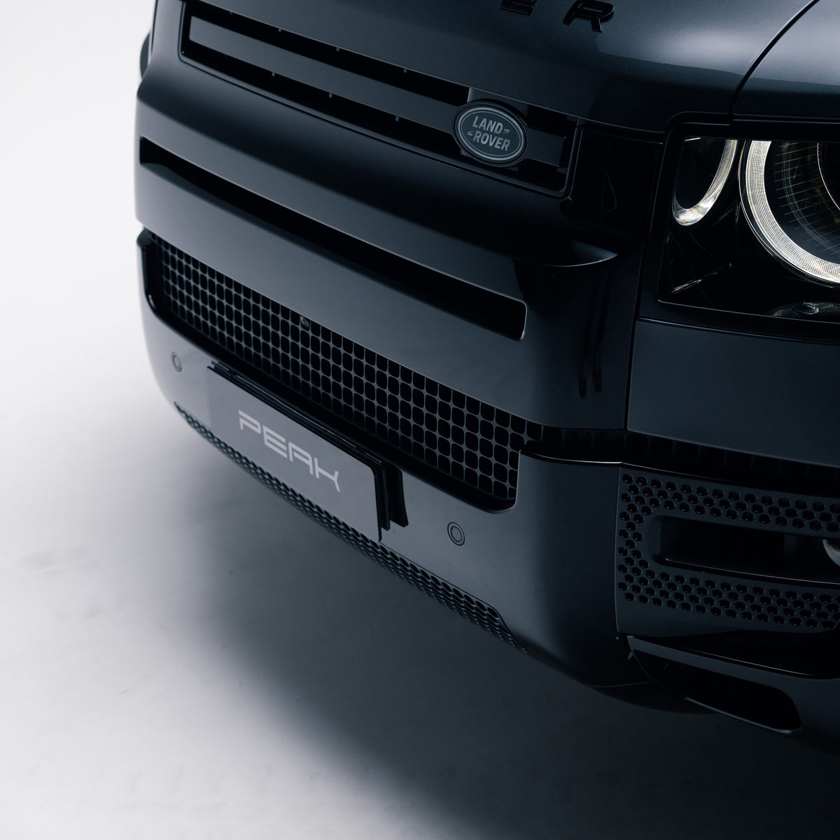 Gloss Black front bumper corner trim on a Land Rover Defender 110, front three-quarter view