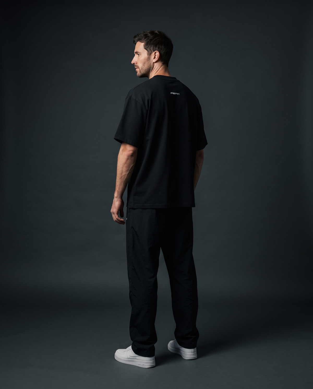 PEAK Back Neck Tee in Black, worn in a dark studio