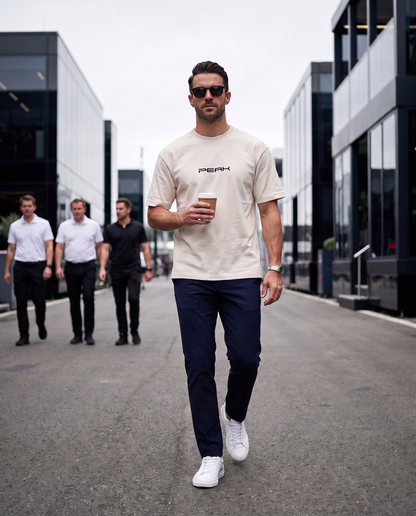 PEAK Heavy Tee in Ecru, worn walking through a race paddock with a coffee