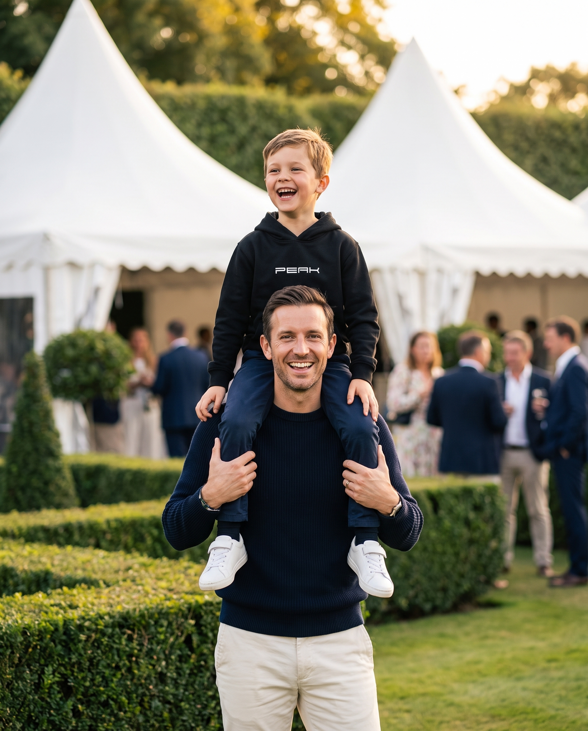 PEAK Kids Hoodie in Black, worn by a boy on his dad's shoulders at a grand prix hospitality garden