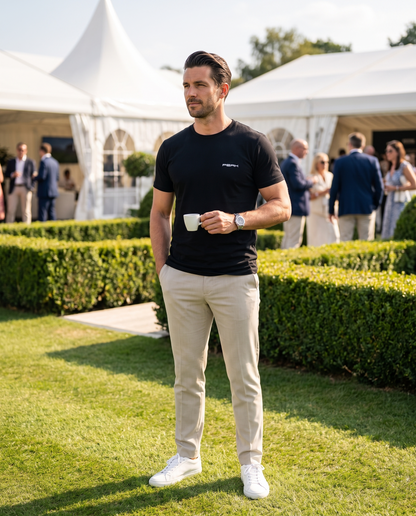 PEAK Tee, Chest & Spine Print in Black, worn on the lawn at a grand prix hospitality garden